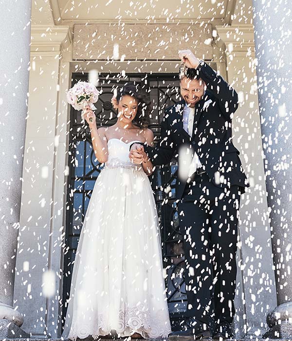 Newly maried couple standing on steps whilst being showered with confetti